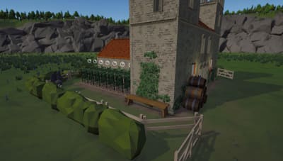 A stone church with ivy on its tower, a bench and stacked wine barrels beside a fenced vineyard on a sunny day